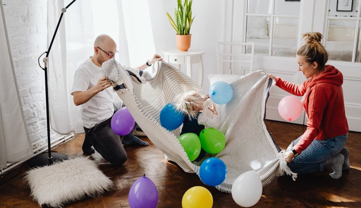 A family enjoying playful moments indoors with balloons and blankets, promoting togetherness and fun.