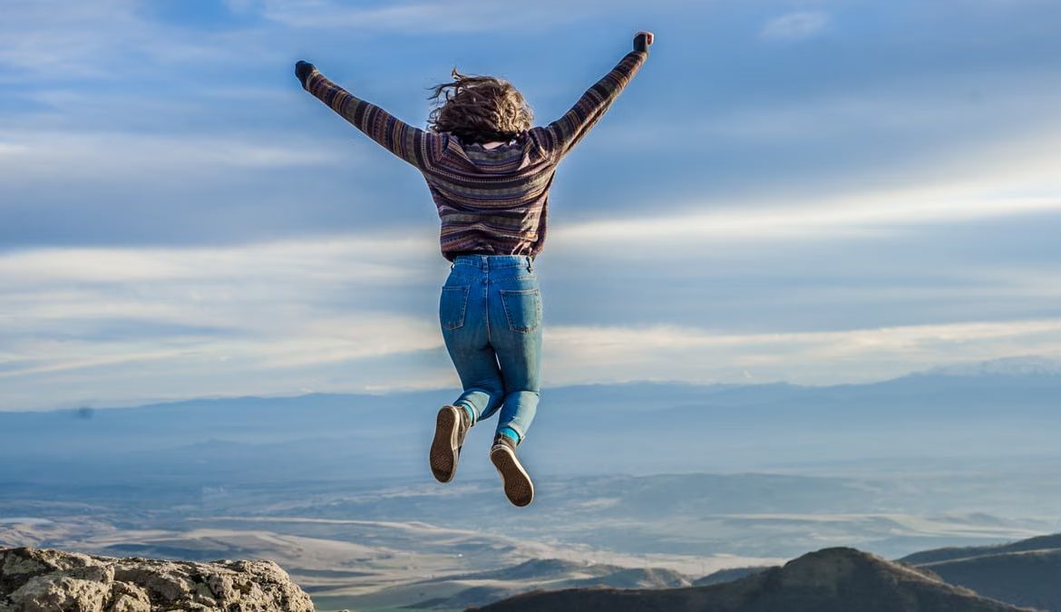 Person jumping on a mountain peak, celebrating adventure and freedom.